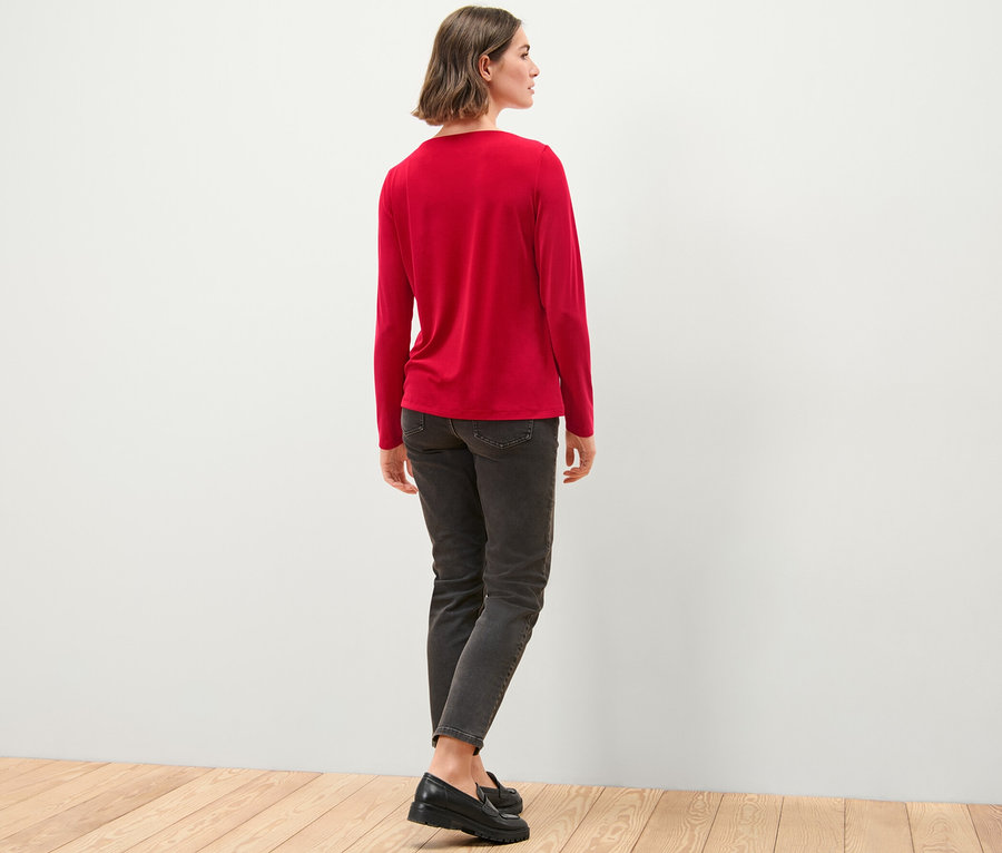 Femme debout, vue de dos, portant une blouse avec fronces, un jean et des chaussures.