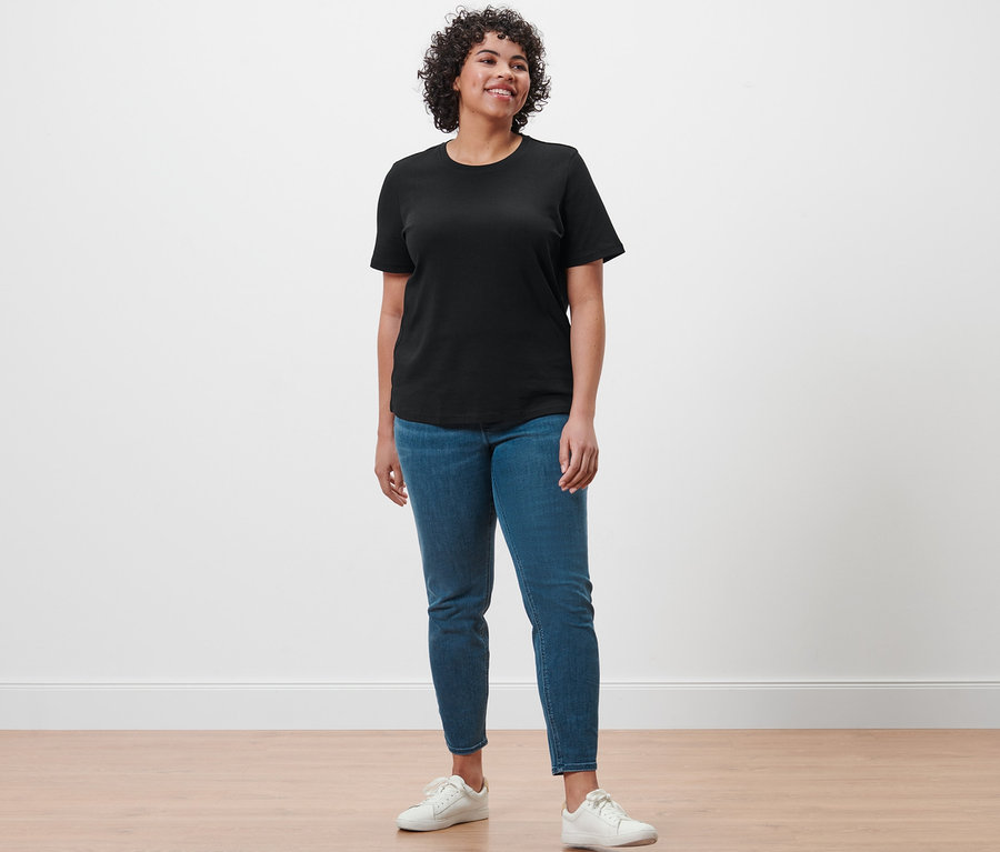 Une femme debout portant un t-shirt basique noir, un tregging « Fit Nelly » et des baskets blanches.