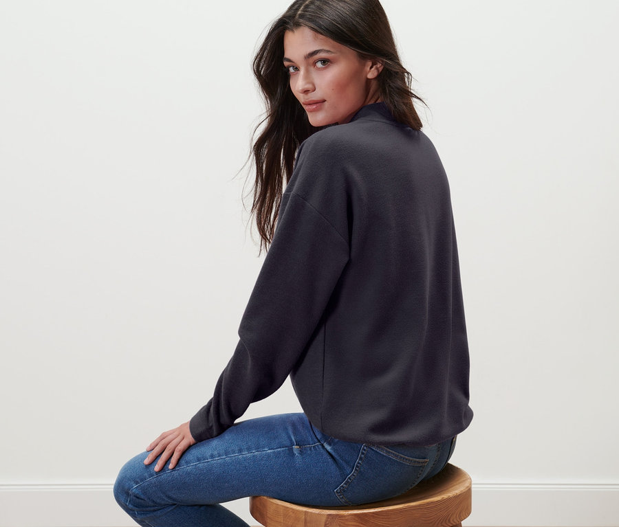 Femme assise sur un tabouret portant un sweat-shirt avec col montant.