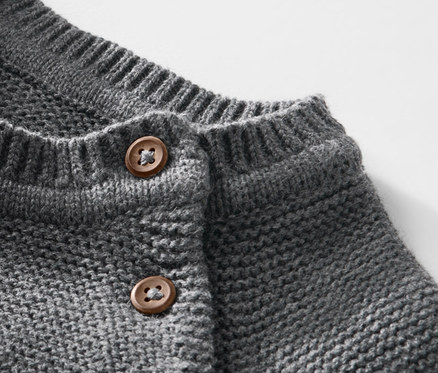 Gros plan sur un pull en maille pour enfant avec des boutons marron.