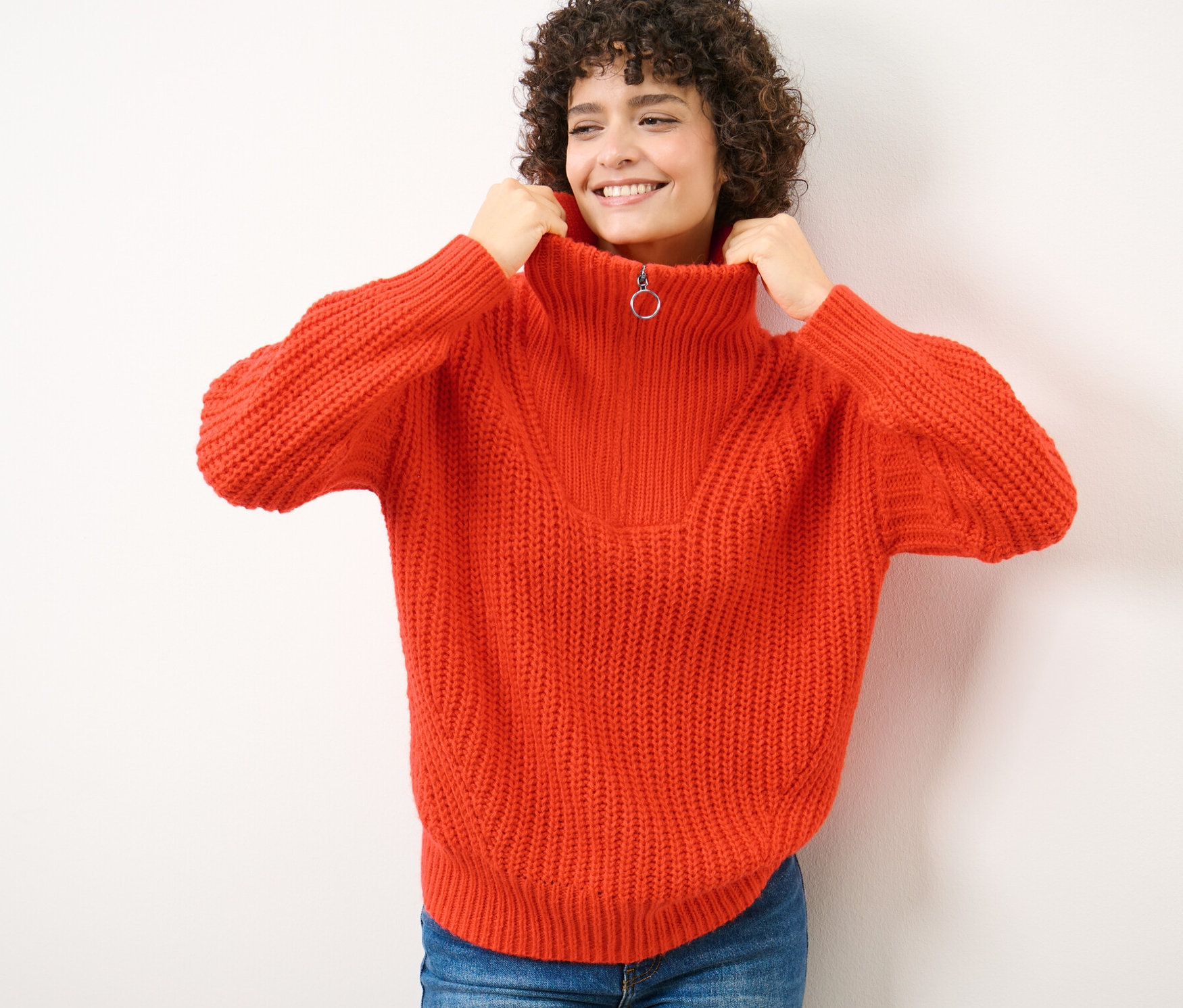 Une femme remonte le col de son pull camionneur orange en grosse maille.