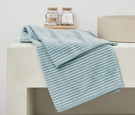 Un linge de bain bleu de haute qualité est plié sur un lavabo blanc à côté de verres avec des cotons-tiges et des boules de coton.