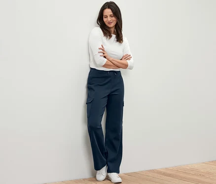 Femme debout contre un mur, portant un pantalon molletonné bleu foncé avec des poches cargo.