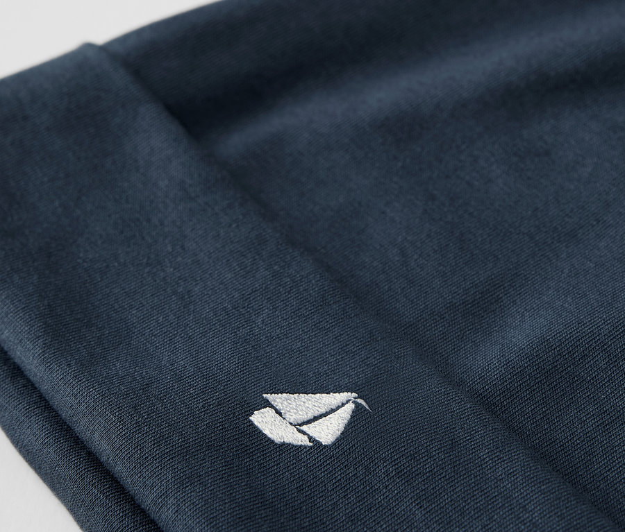 Gros plan sur un bonnet en tissu bleu d'un ensemble pour bébé, avec un logo blanc brodé.
