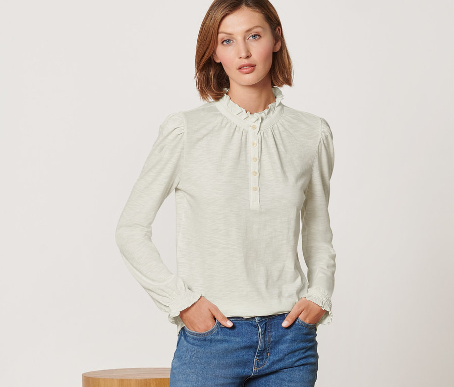 Une femme pose en T-shirt manches longues avec fronces et un jean.