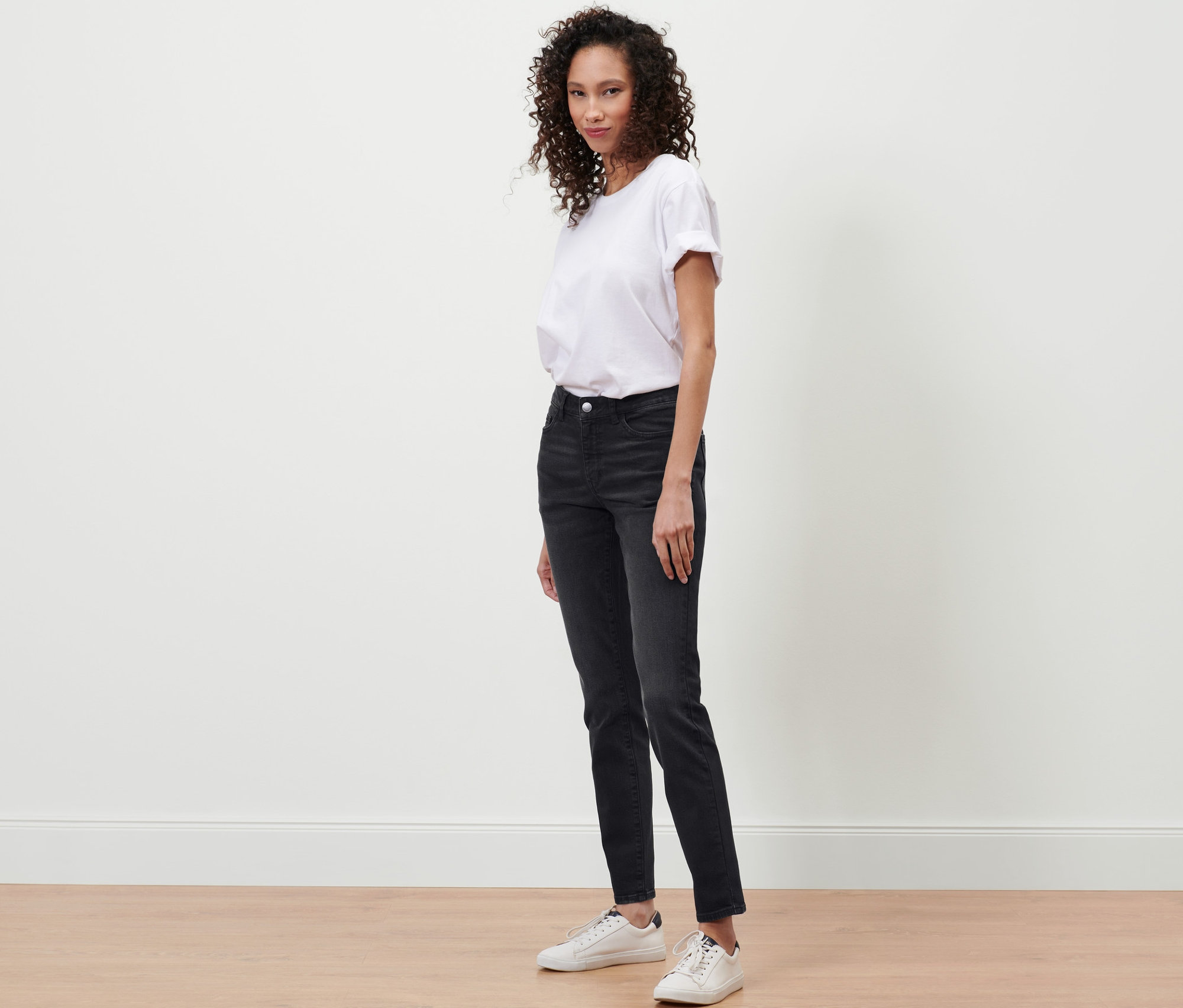Une femme debout portant un jean slim en denim « Fit Emma » noir et un t-shirt blanc.