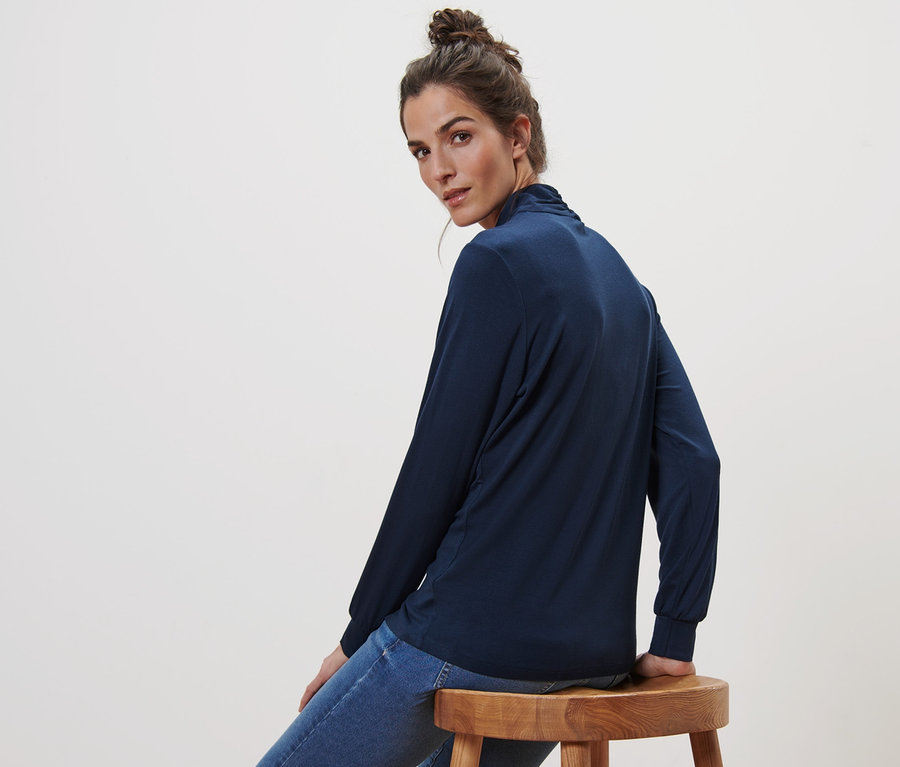 Femme assise sur un tabouret portant un t-shirt bleu foncé à manches longues avec encolure en V.