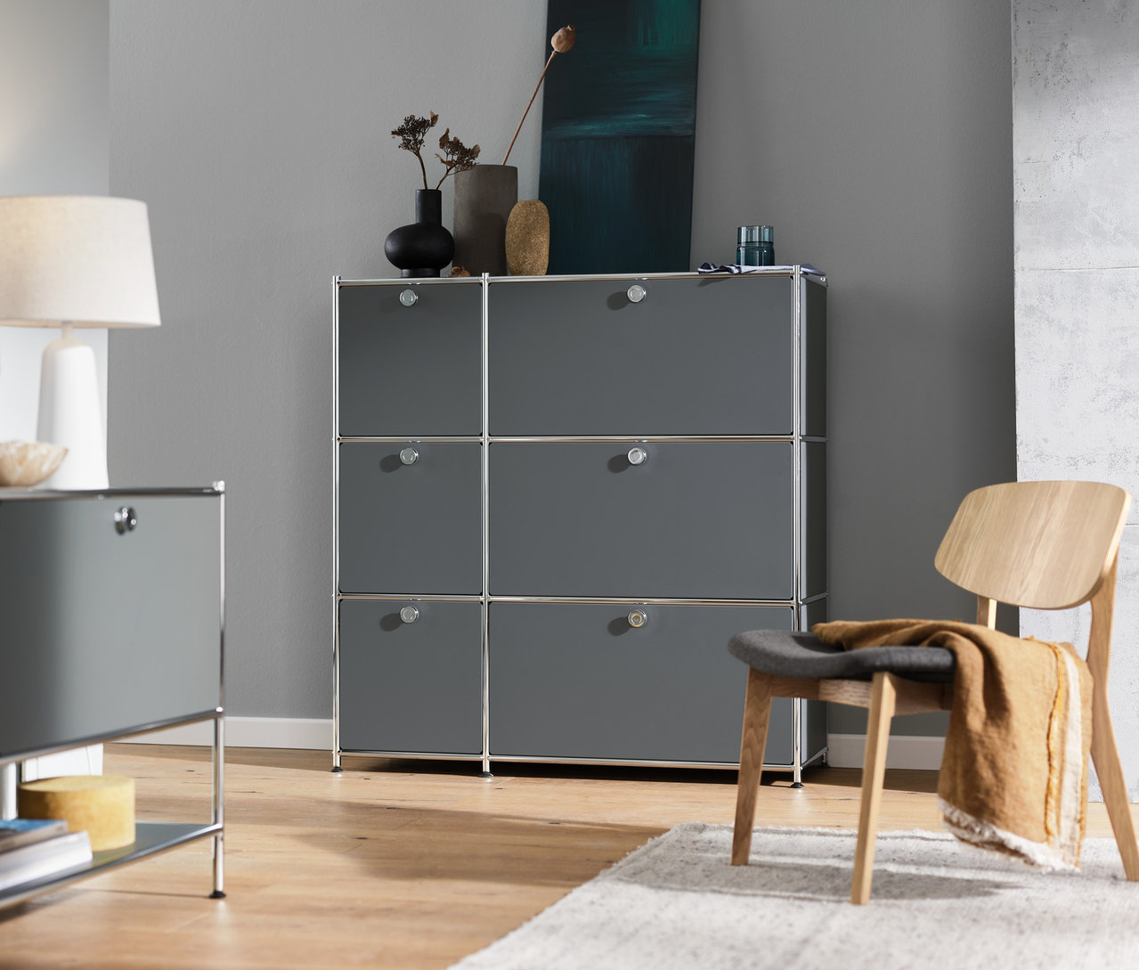 Intérieur avec commode grise « CN3 » à 6 abattants, buffet bas gris « CN3 » à 1 abattant, lampe de table blanche et chaise d'intérieur.