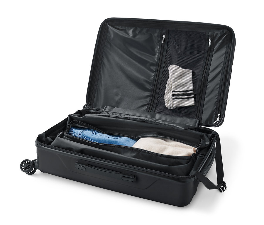 Valise rigide noire de taille moyenne ouverte avec des vêtements à l'intérieur.