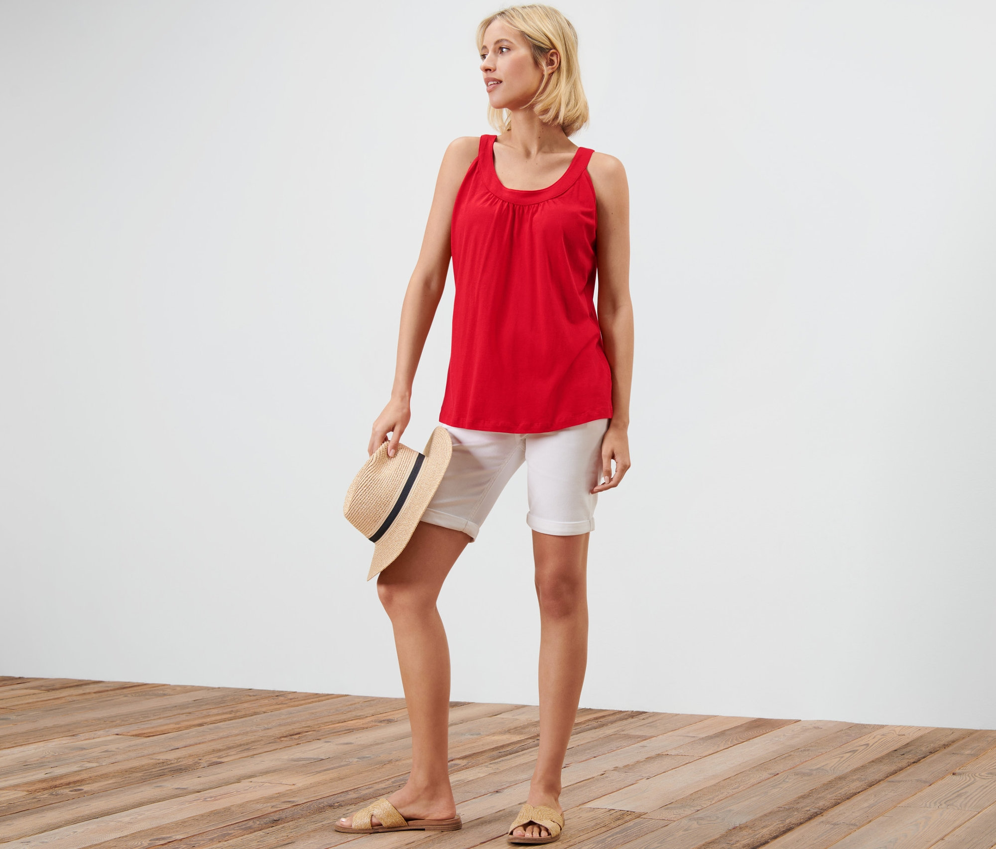 Femme tenant un chapeau et portant un haut rouge et un short blanc.