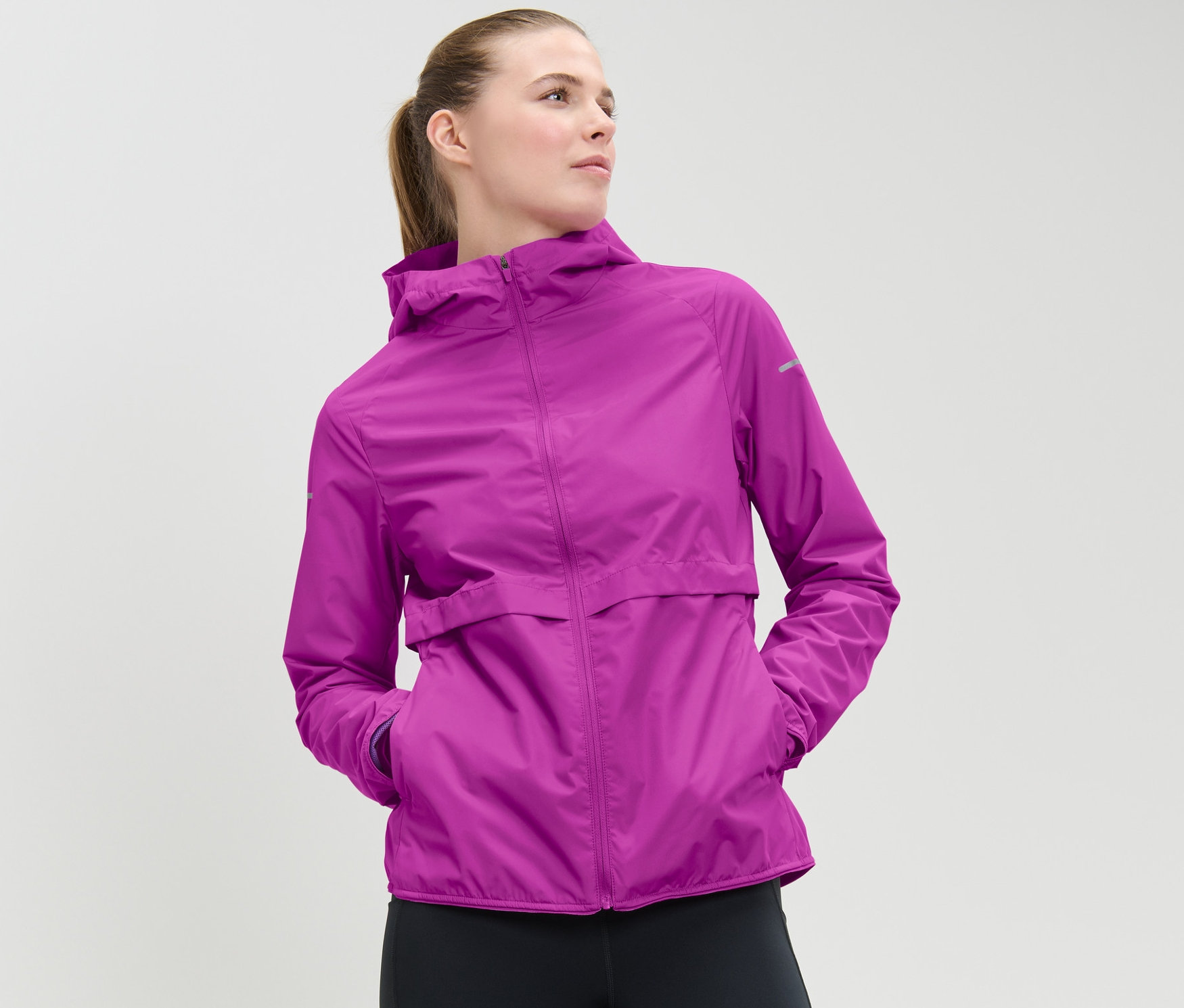 Femme portant une veste de course coupe-vent rose baie fluo et un legging noir.