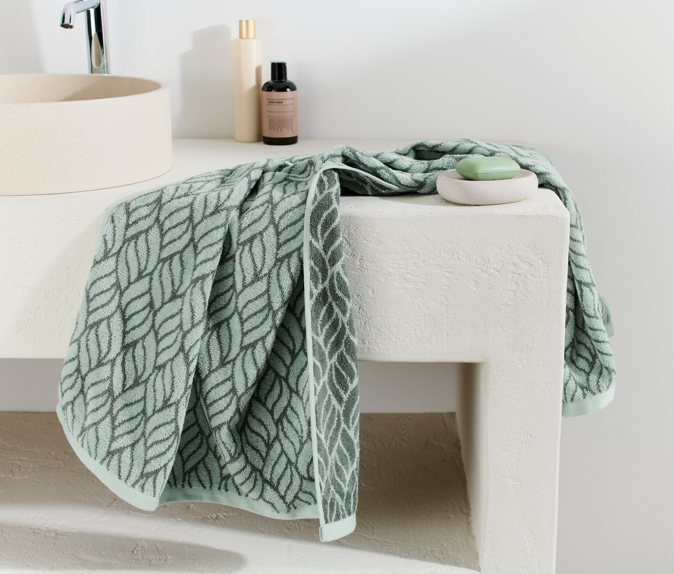 Un drap de bain en jacquard à motif de feuilles est posé sur un lavabo blanc.
