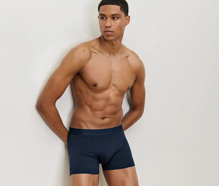 Un homme appuyé contre un mur porte un 4 boxers bleus.