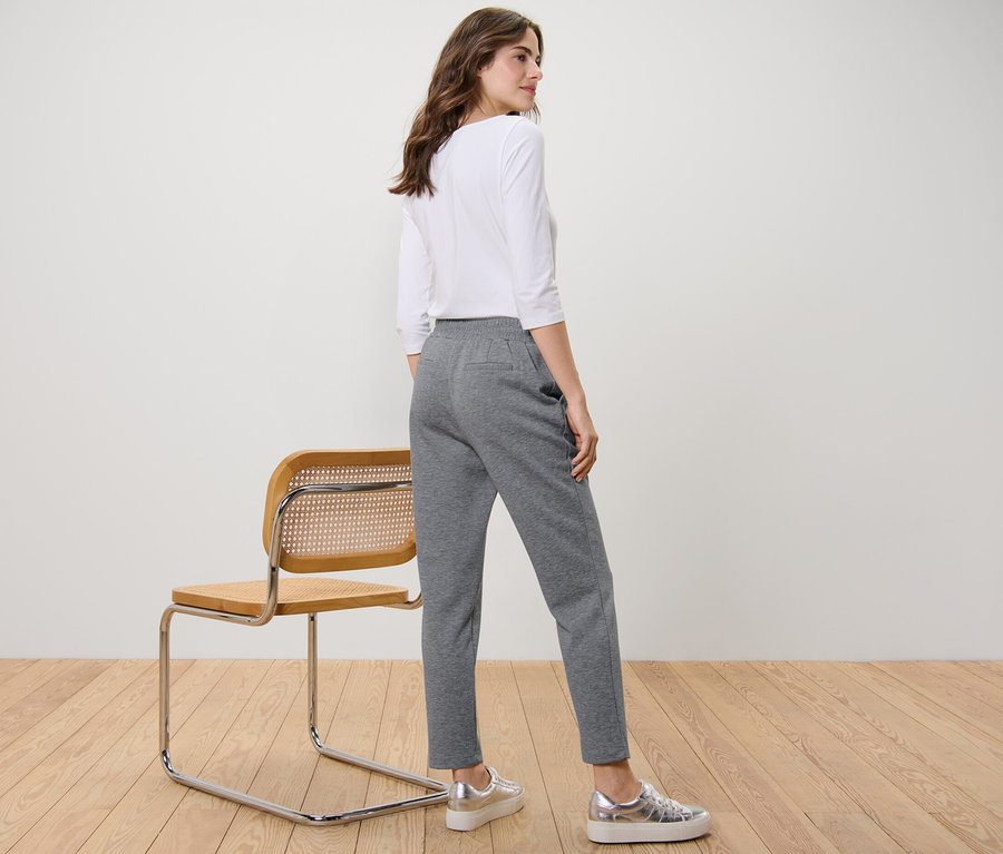 Une femme se tient de côté et porte un pantalon de jogging gris.