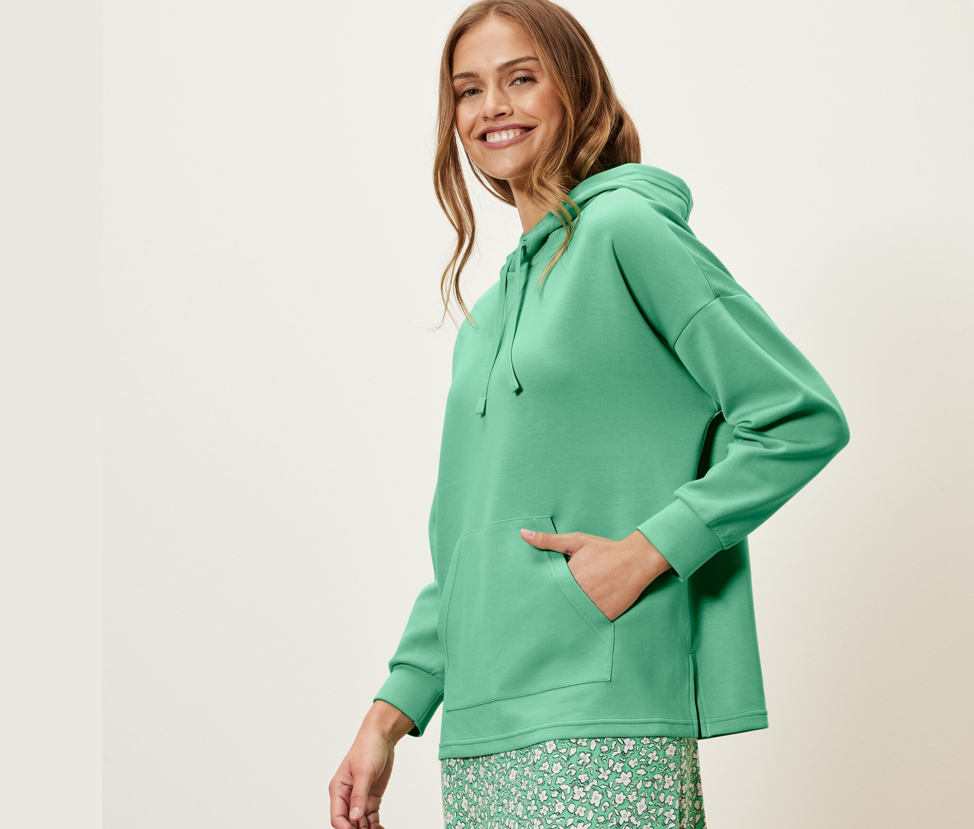 Femme posant en pull à capuche vert en mélange de modal et jupe fleurie verte.