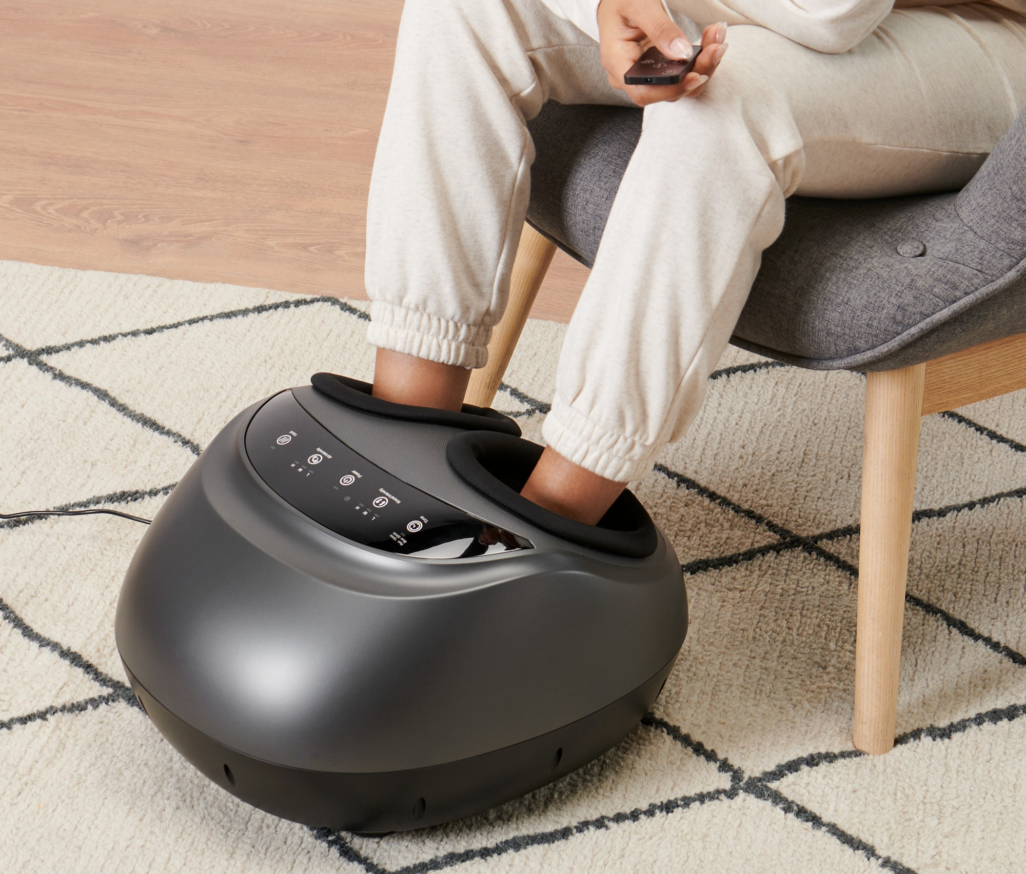 Une femme est assise dans un fauteuil et utilise un appareil de massage des pieds.