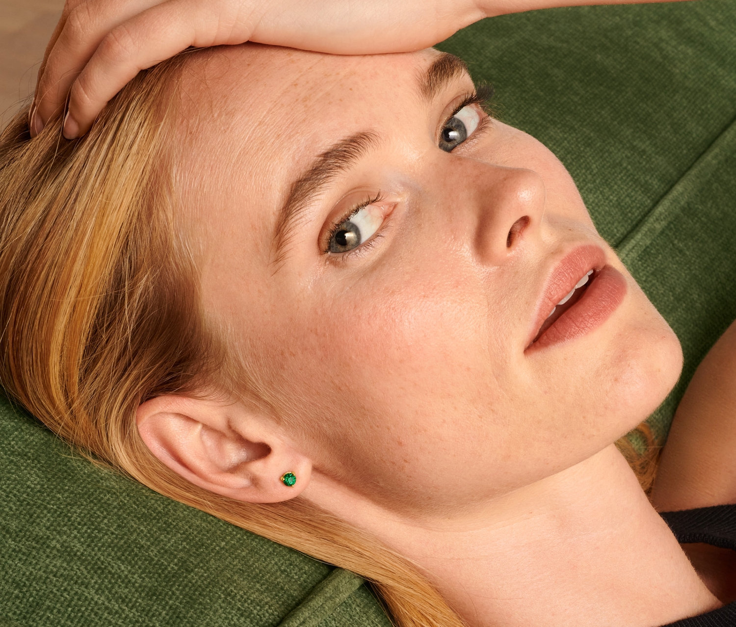Une femme blonde est allongée sur un canapé vert et porte un ensemble de clous d'oreilles.