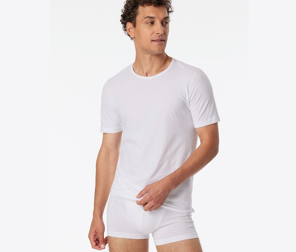 Un homme porte 2 t-shirts blancs SCHIESSER en coton bio.