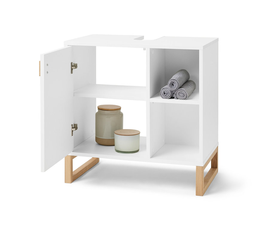 Meuble sous-vasque blanc ouvert avec porte et compartiment latéral. Dans le compartiment latéral, il y a des serviettes grises enroulées et à l'intérieur du meuble, il y a des bougies et une boîte.