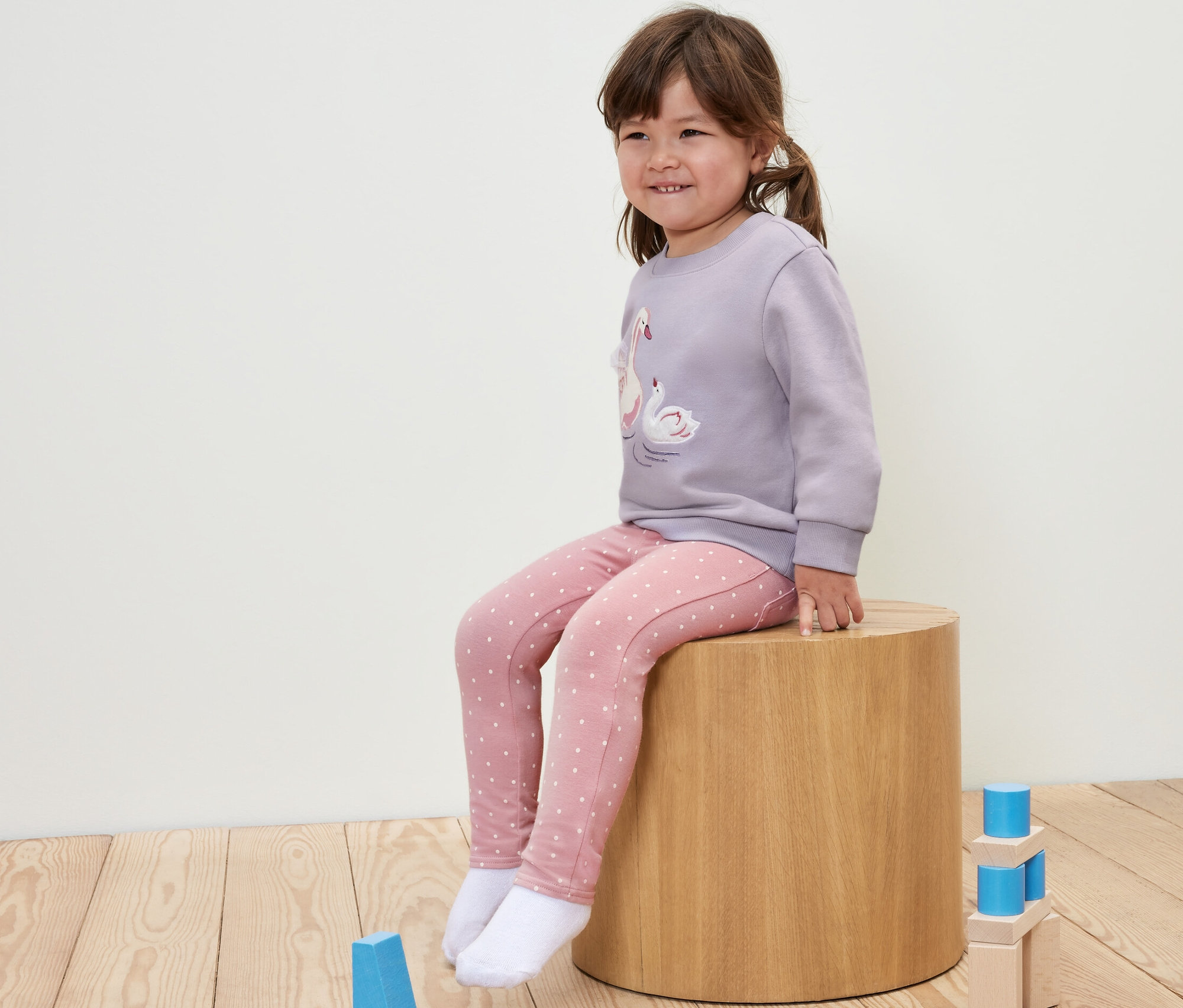 Fillette assise sur un tabouret en bois portant un jegging pour enfant – Fit « Ida » à pois.