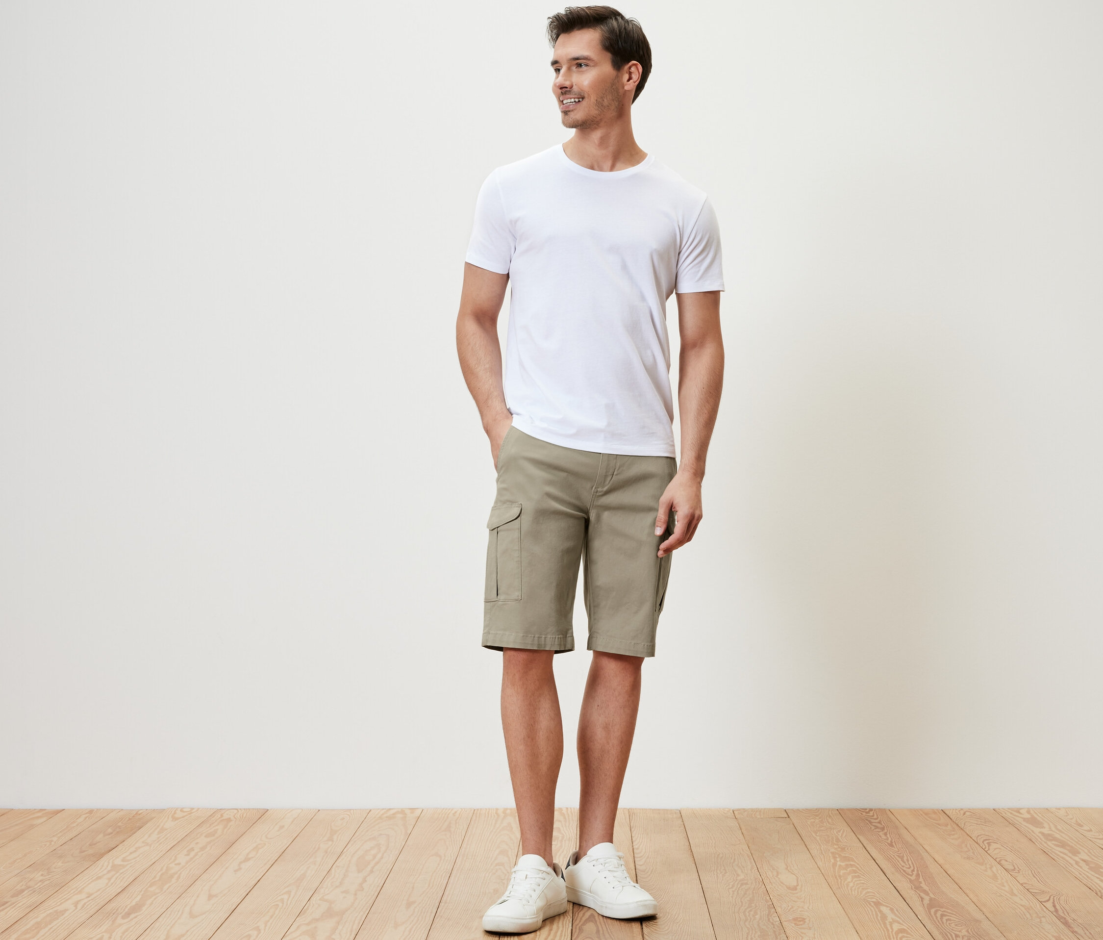Un homme debout portant un short cargo beige et un t-shirt blanc.
