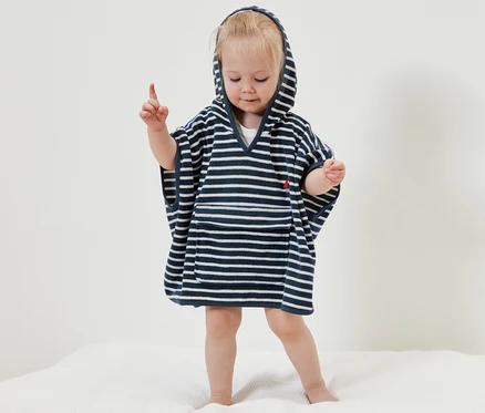Une petite fille se tient debout sur une couverture blanche et porte un poncho en éponge sur le thème de la mer.