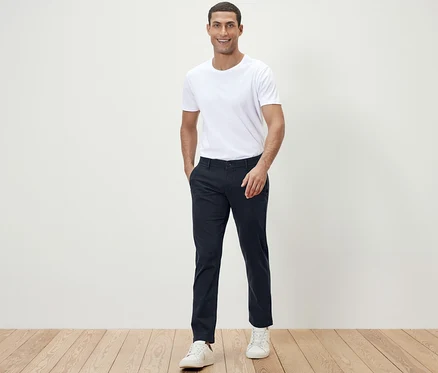 Un homme pose face à la caméra en t-shirt blanc et pantalon chino bleu foncé.