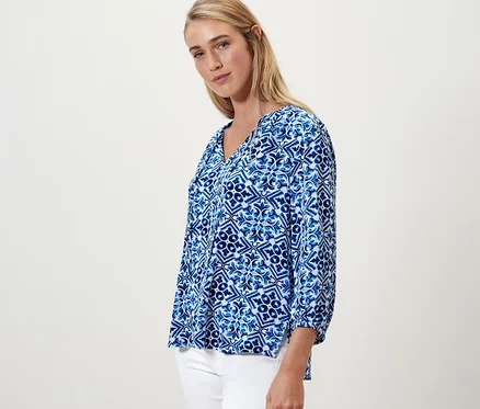 Femme blonde posant en chemisier-tunique bleu imprimé.