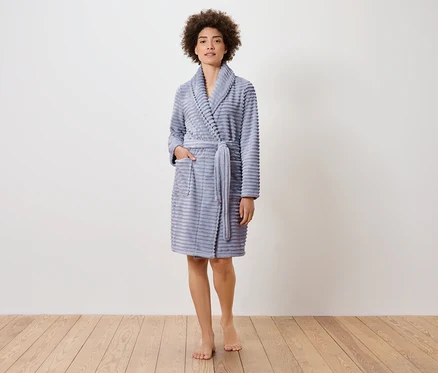 Une femme se tient sur un plancher en bois et porte un peignoir bleu.