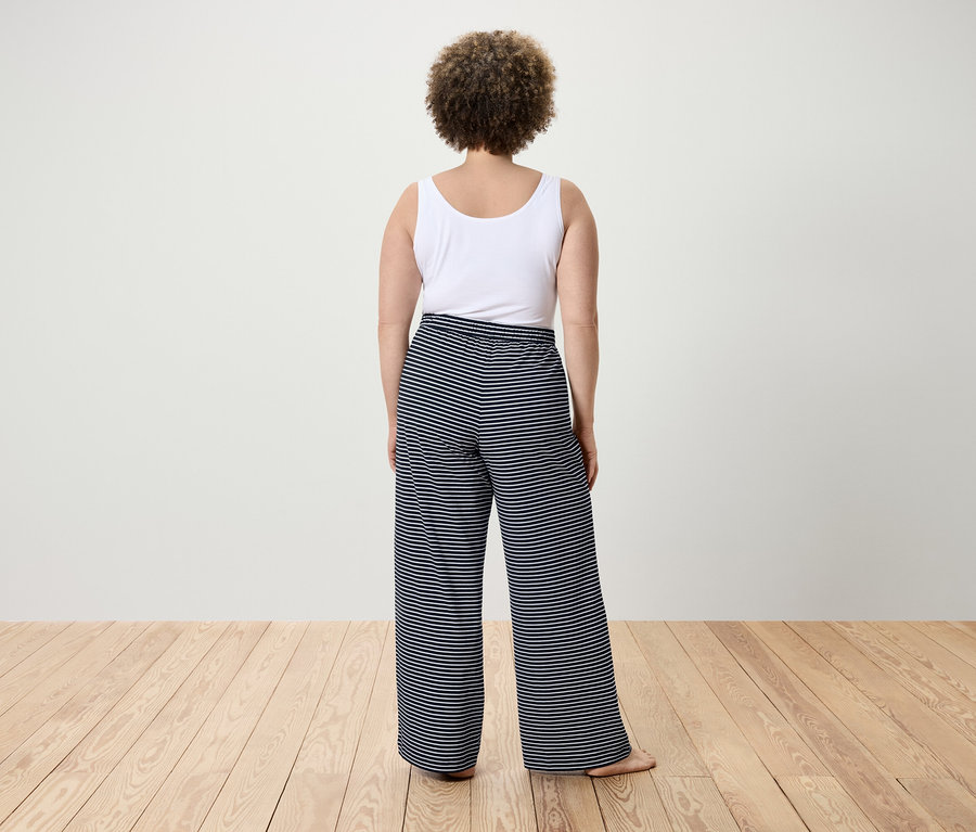 Vue de dos d'une femme aux cheveux bouclés portant un débardeur blanc et un pantalon rayé.