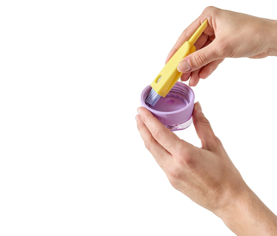 Des mains trempent un pinceau jaune dans de la peinture violette dans un récipient.