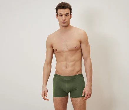 Un homme torse nu pose en caleçon boxer vert olive.