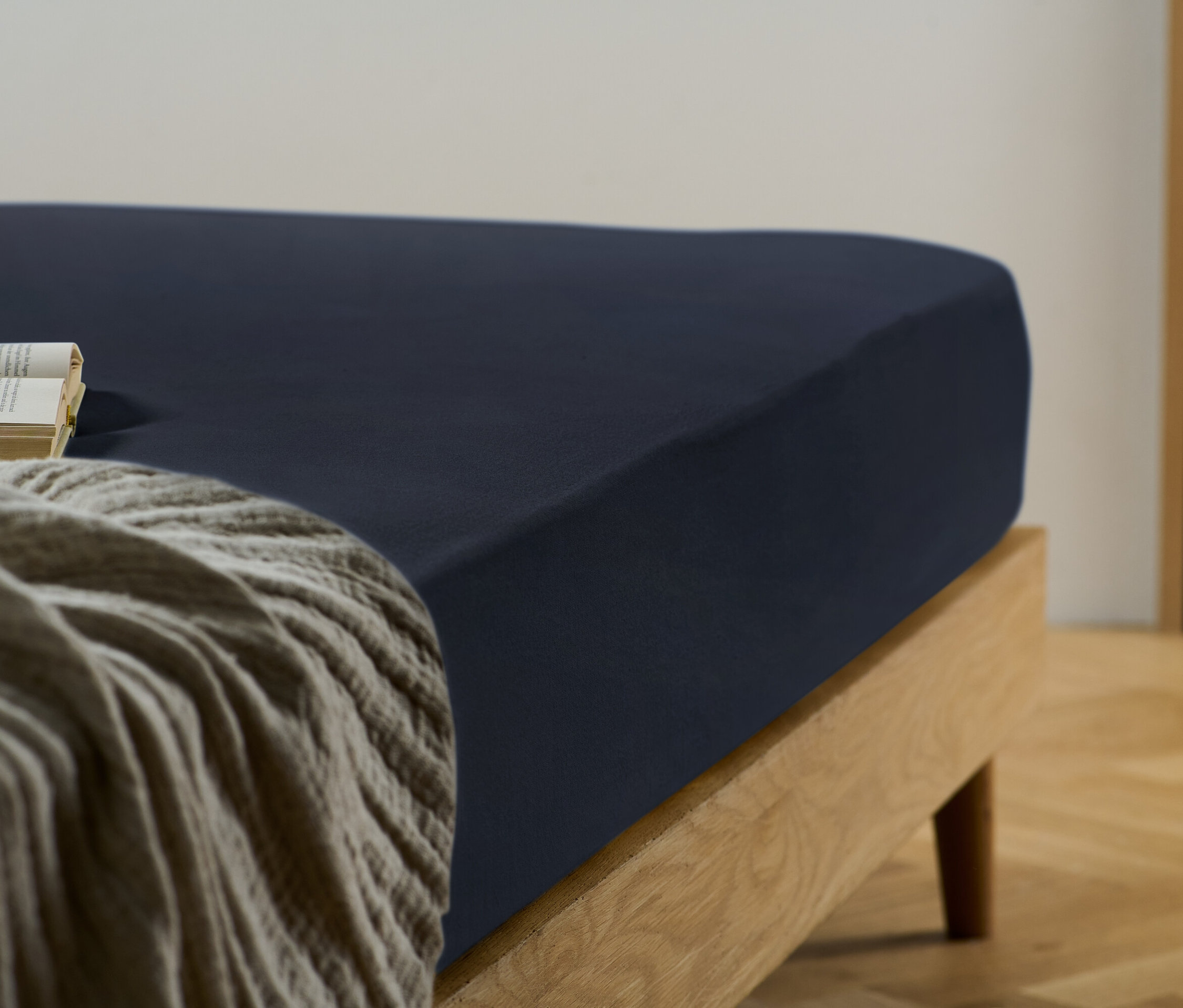Gros plan d'un drap-housse bleu sur un lit avec un cadre en bois, avec un livre posé sur une couverture beige.