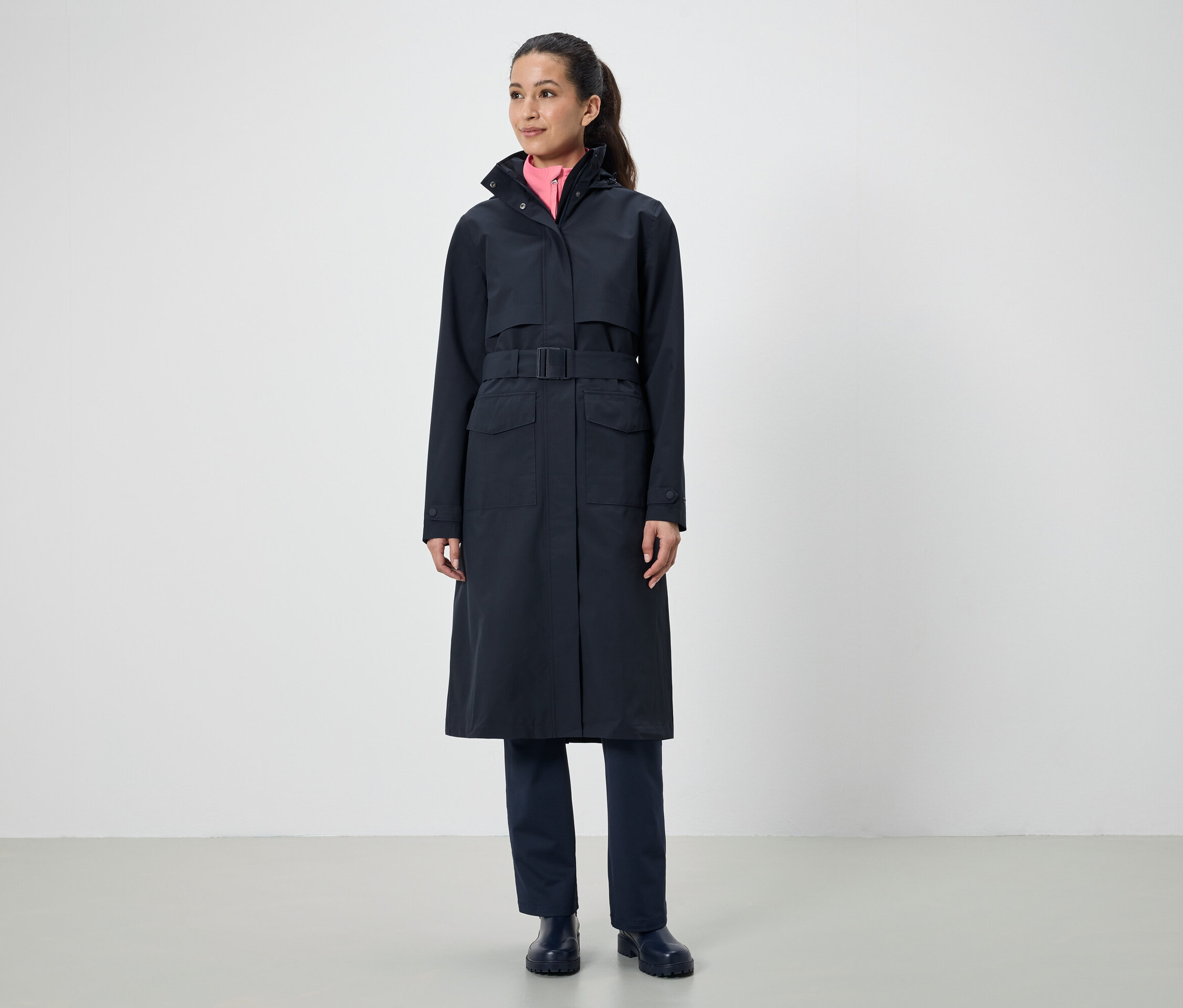 Une femme porte un long manteau noir avec une ceinture.