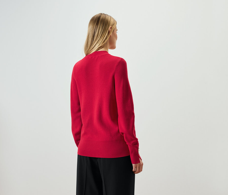 Vue de dos, femme aux cheveux blonds portant un pull rouge et un pantalon noir.