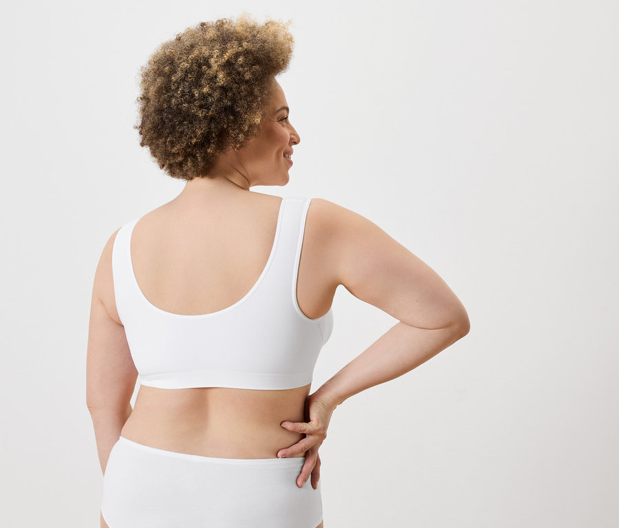 Une femme aux cheveux bouclés pose de dos, portant un soutien-gorge et une culotte blancs.