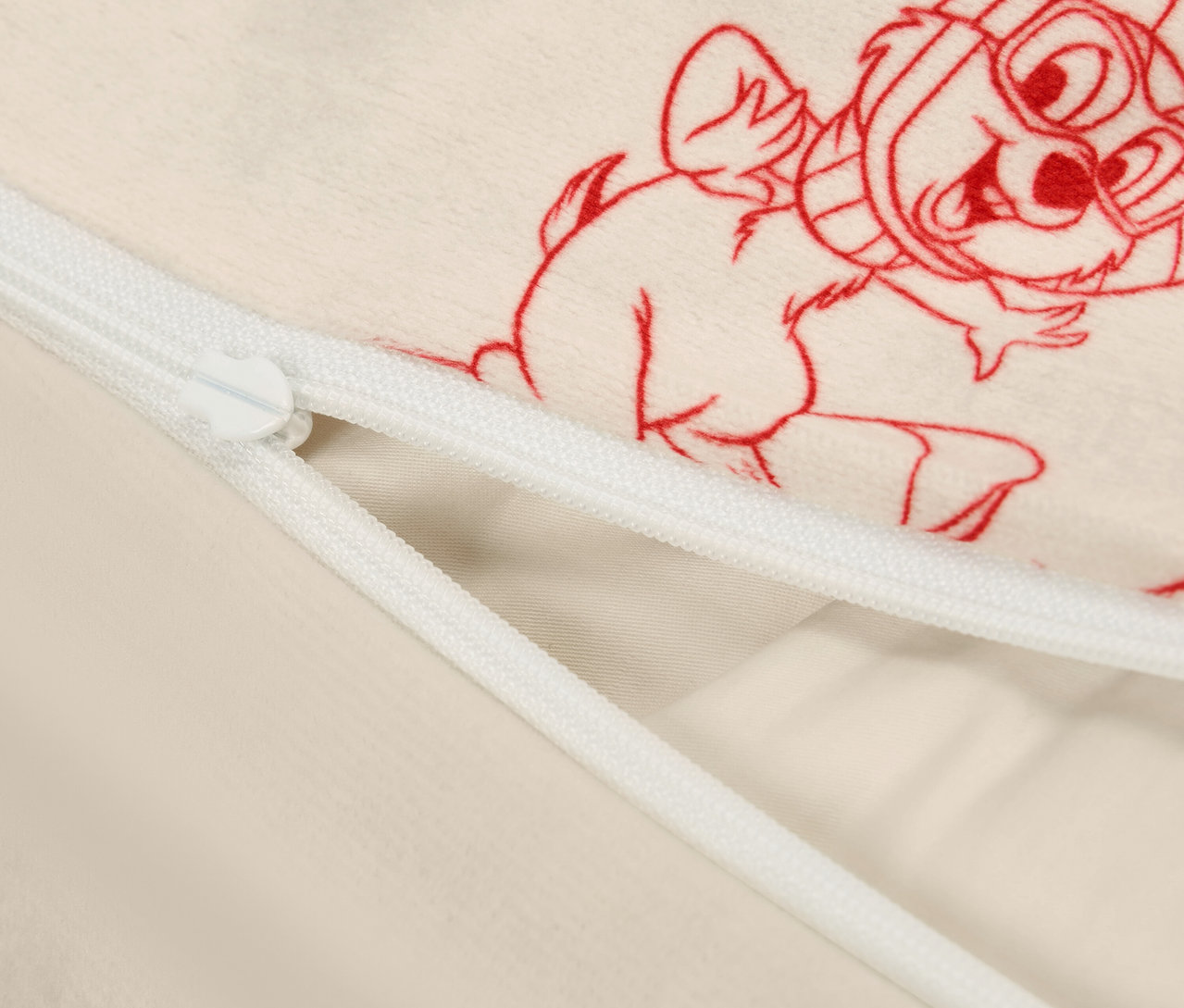 Détail d'une housse en tissu beige avec fermeture éclair et imprimé rouge de personnage de dessin animé.