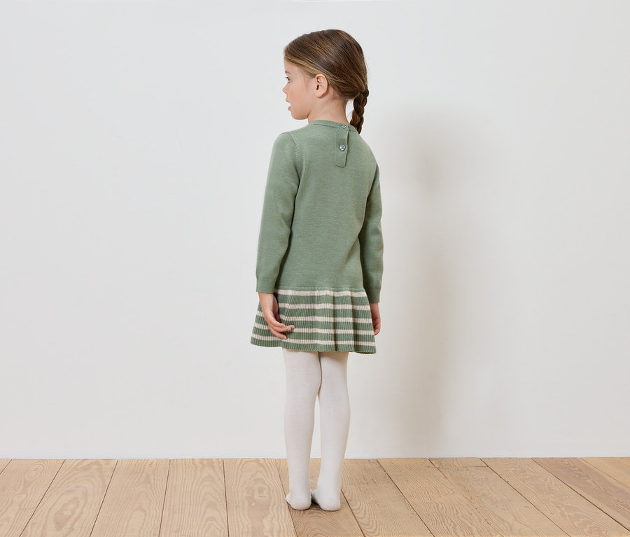 Une fille en robe tricotée verte se tient dos à la caméra.