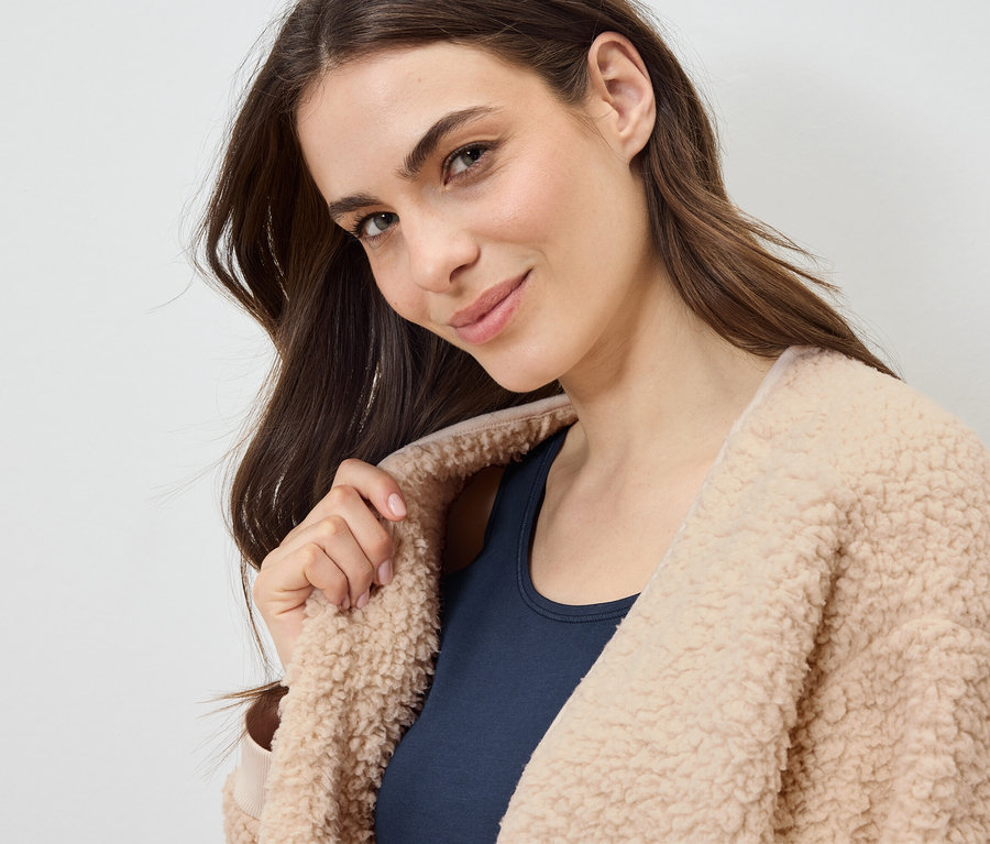 Portrait d'une femme aux cheveux bruns portant un manteau beige duveteux sur un haut bleu marine.