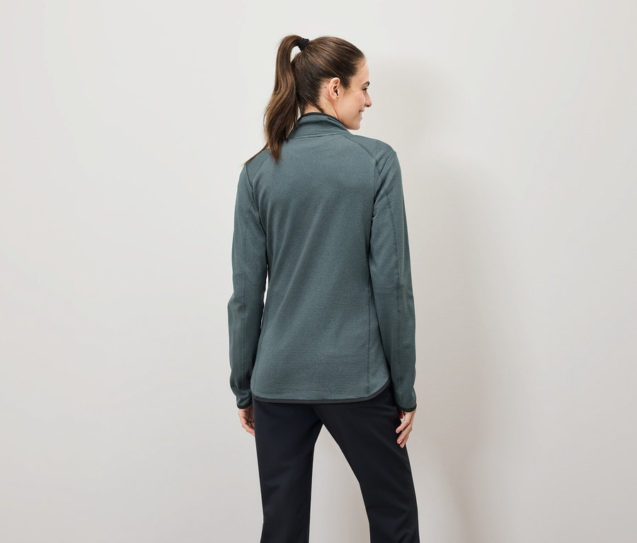 Vue de dos, une femme aux cheveux bruns attachés en queue de cheval porte un sweat-shirt vert zippé et un pantalon noir.