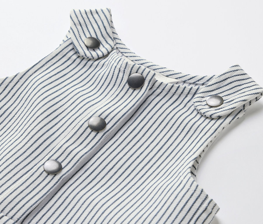 Gros plan sur une salopette tissée pour enfants avec des rayures bleues et des boutons argentés.