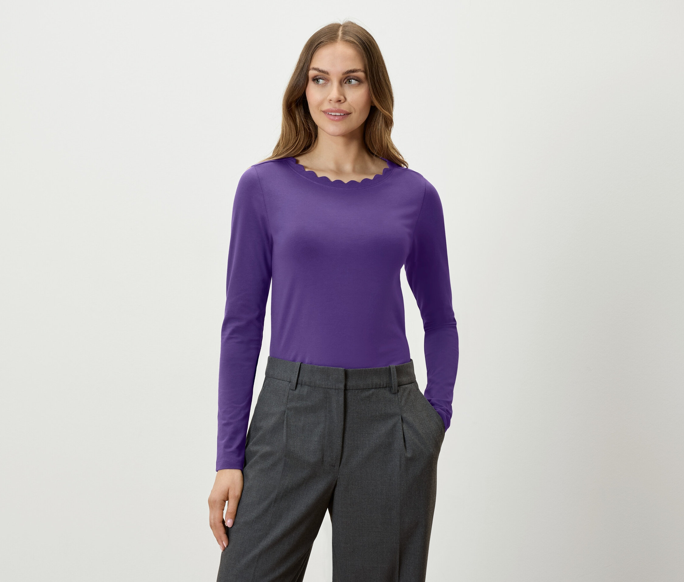Une femme porte un t-shirt violet à manches longues et un pantalon gris.