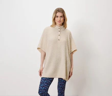 Une femme pose en studio sur un fond blanc. Elle porte un pull beige et un legging bleu.