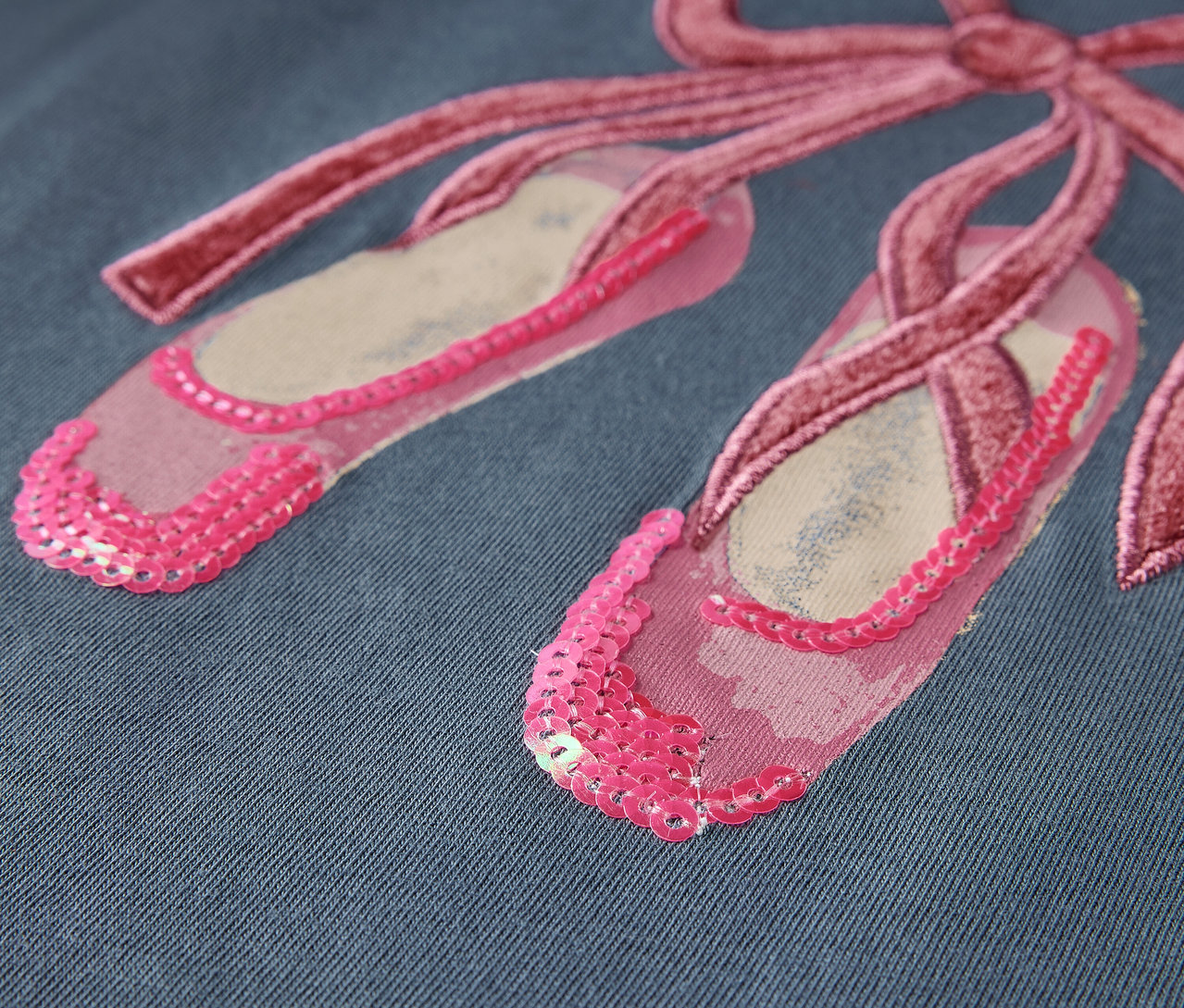 Gros plan de chaussons de ballet roses avec un nœud sur un fond bleu.