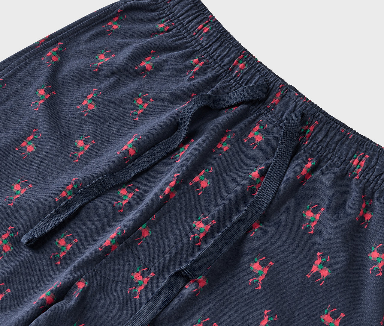 Détail d'un pantalon de pyjama bleu avec des rennes rouges et des selles vertes.