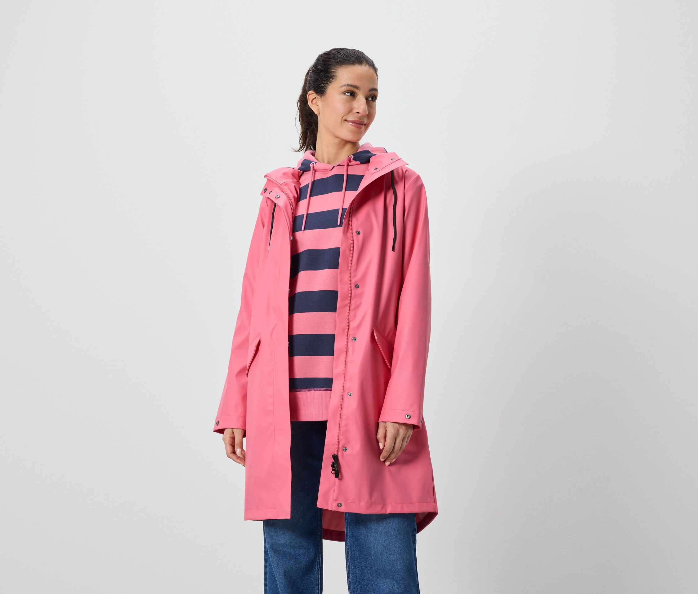 Une femme porte un manteau rose et un sweat à capuche rayé.