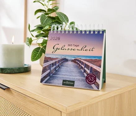Sur une commode se trouvent un calendrier avec l'inscription Gelassenheit, une bougie et une plante.