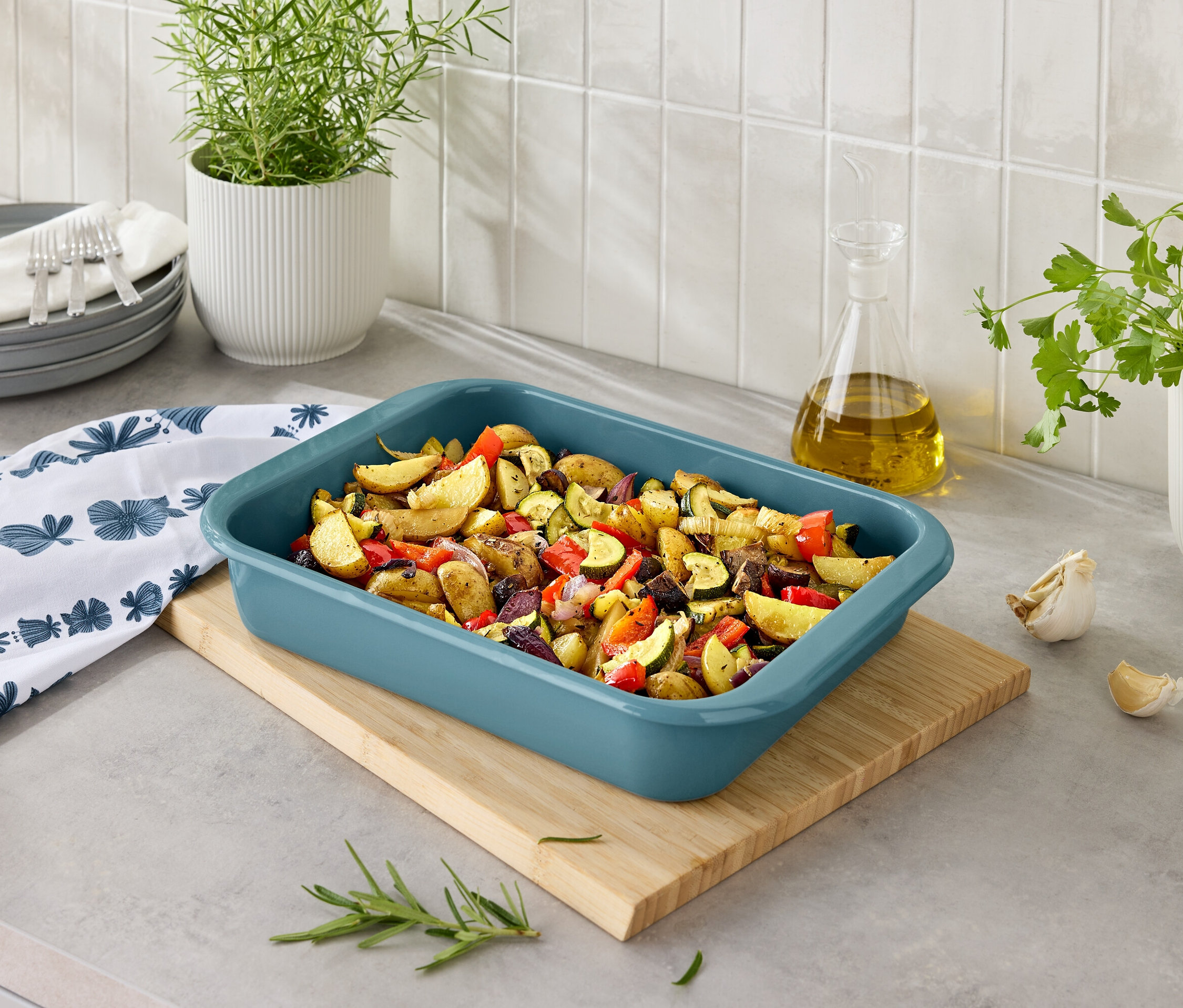 Pommes de terre et légumes cuits au four dans un plat bleu sur une planche à découper en bois.