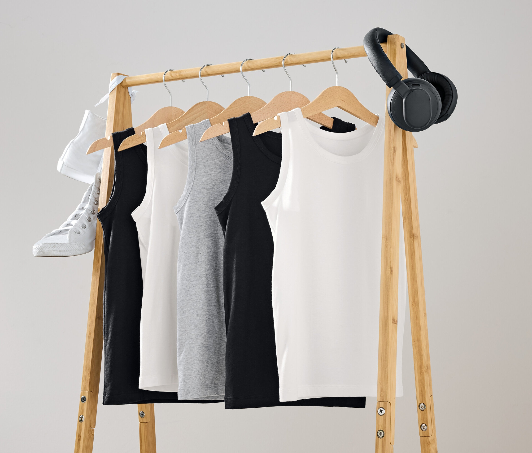 Des débardeurs noirs, blancs et gris sont suspendus à un portant en bois. Une chaussure blanche et un casque noir sont suspendus au portant.