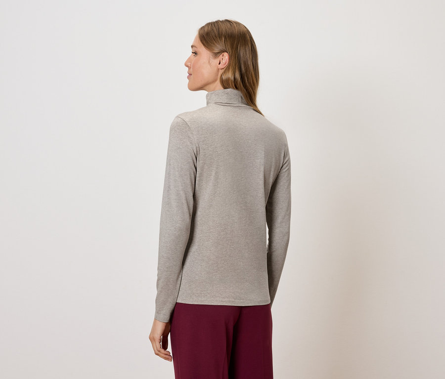 Une femme, vue de dos, porte un pull à col roulé beige et un pantalon bordeaux.